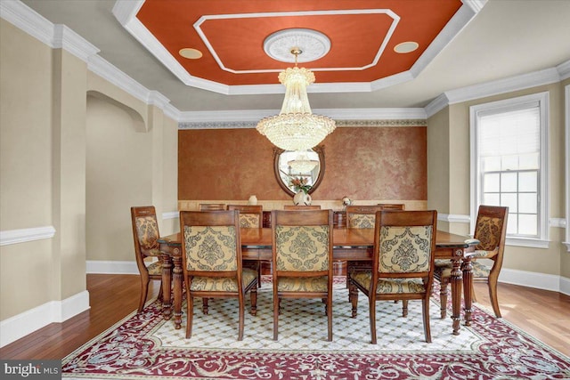 dining space featuring a chandelier, ornamental molding, a raised ceiling, and hardwood / wood-style floors