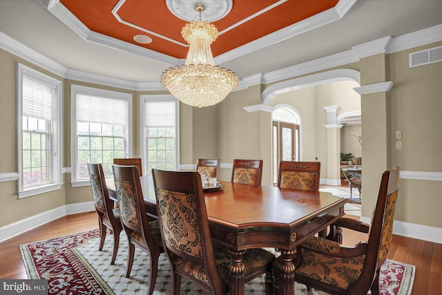 dining room with decorative columns, hardwood / wood-style floors, an inviting chandelier, and a tray ceiling