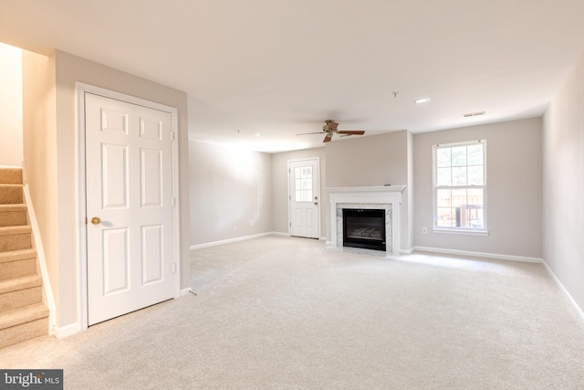 unfurnished living room with light carpet, a high end fireplace, and ceiling fan