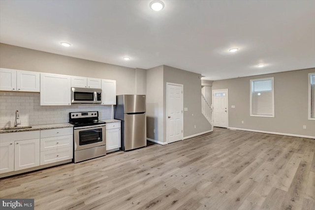 kitchen with sink, stainless steel appliances, light stone counters, tasteful backsplash, and white cabinets