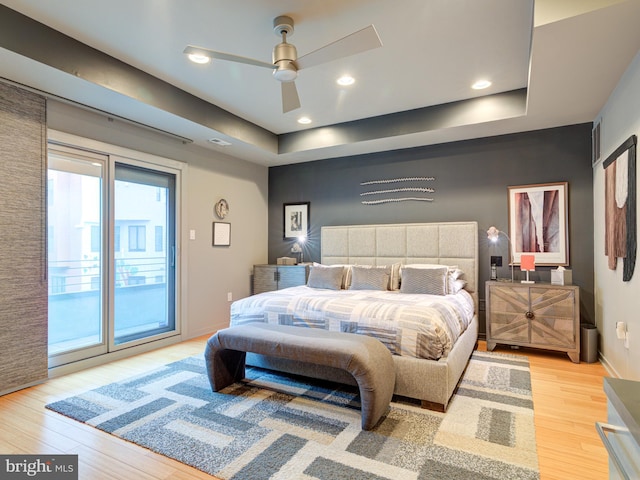 bedroom with a raised ceiling, access to outside, and light hardwood / wood-style flooring