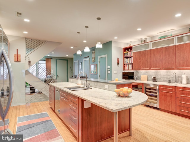 kitchen with a kitchen island with sink, sink, pendant lighting, and beverage cooler