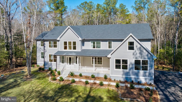 view of front of house featuring covered porch, a shingled roof, and a front lawn