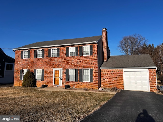 colonial house with brick siding, a chimney, a garage, and a front yard