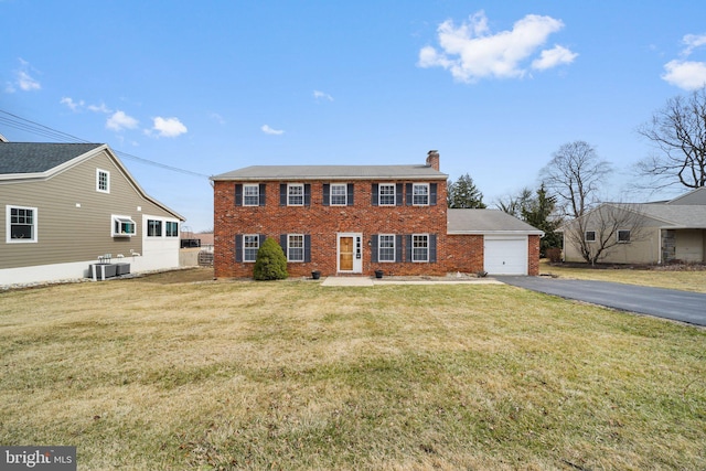 colonial inspired home with brick siding, driveway, a chimney, and a front yard