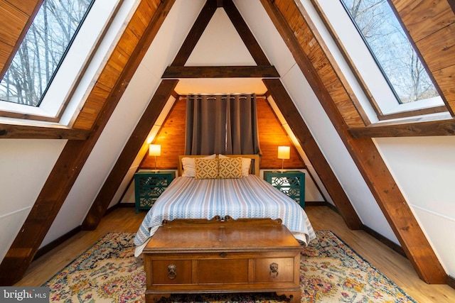 bedroom featuring lofted ceiling with skylight, light wood-style floors, and wooden walls