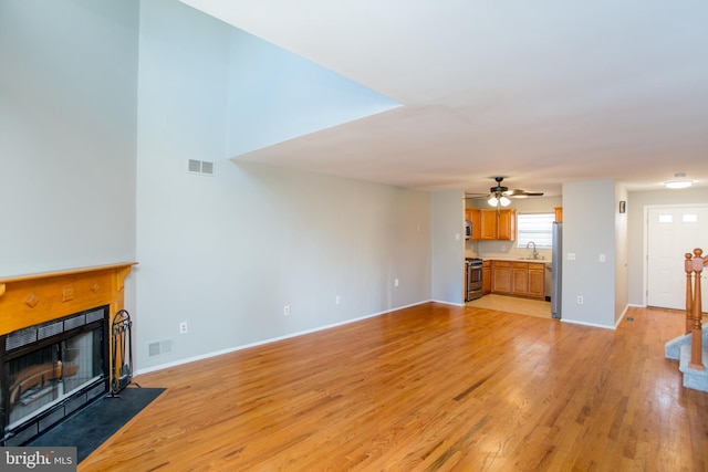 unfurnished living room with sink, ceiling fan, and light hardwood / wood-style flooring