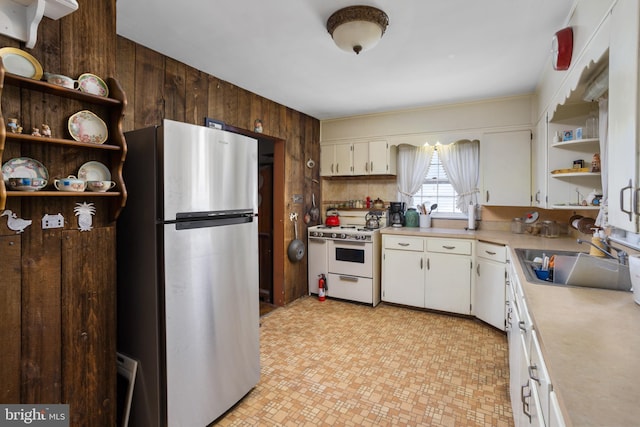 kitchen with stainless steel refrigerator, wood walls, white cabinetry, sink, and white gas range oven