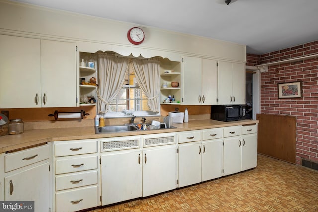 kitchen with sink, white cabinets, and brick wall