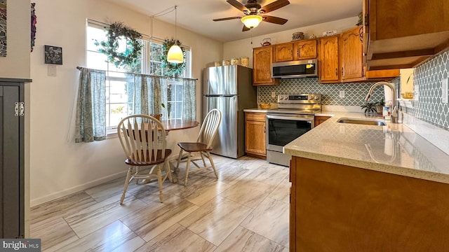 kitchen featuring sink, light stone counters, hanging light fixtures, appliances with stainless steel finishes, and decorative backsplash