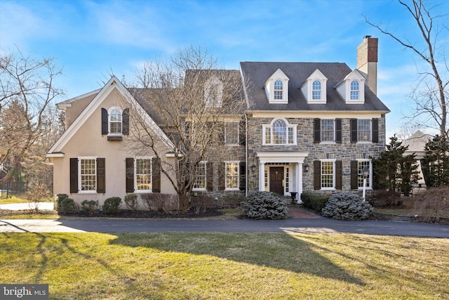 colonial inspired home with stone siding, a chimney, and a front yard