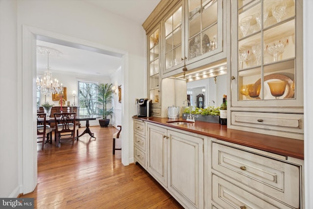 bar with baseboards, a sink, crown molding, light wood-style floors, and a notable chandelier