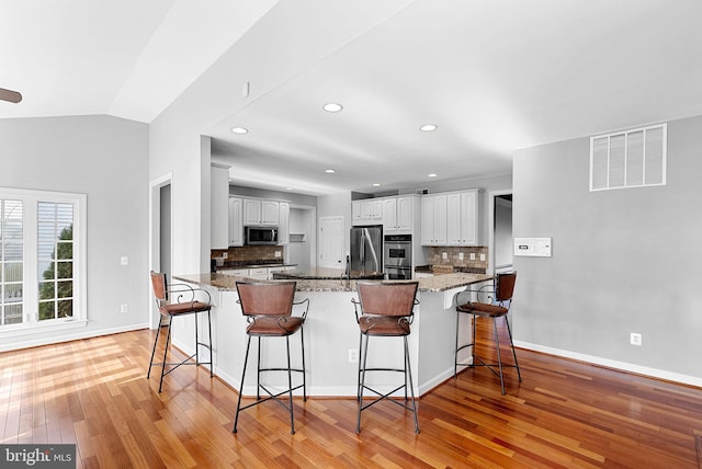 kitchen featuring dark stone countertops, a breakfast bar area, white cabinets, kitchen peninsula, and stainless steel appliances