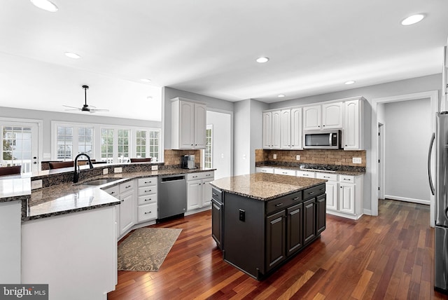 kitchen with sink, white cabinetry, appliances with stainless steel finishes, a kitchen island, and dark stone counters