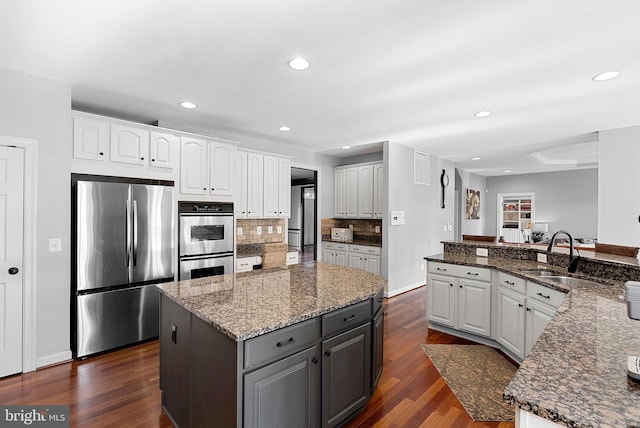 kitchen with sink, a center island, dark stone countertops, stainless steel appliances, and white cabinets