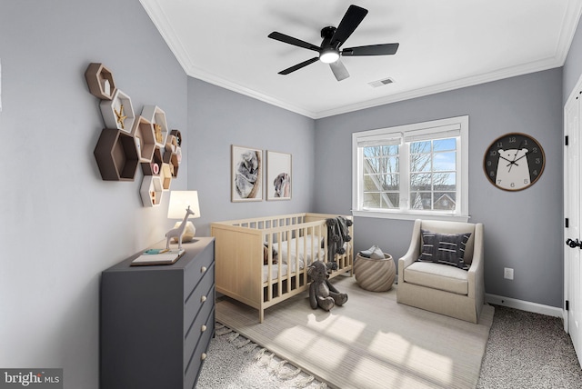 carpeted bedroom with a crib, crown molding, and ceiling fan