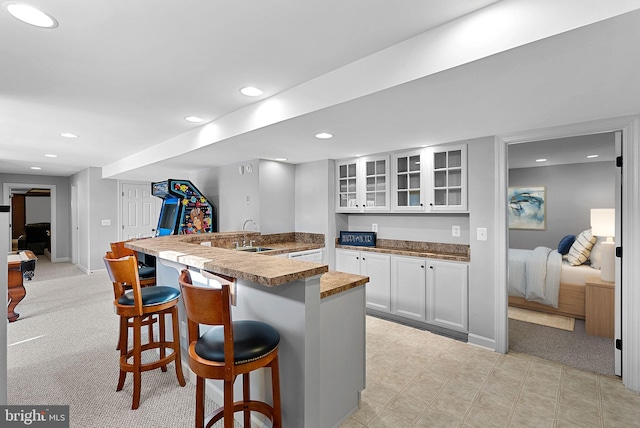 kitchen featuring a kitchen bar, sink, kitchen peninsula, light colored carpet, and white cabinets