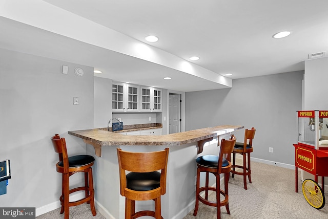 kitchen featuring a breakfast bar, white cabinetry, sink, light colored carpet, and kitchen peninsula