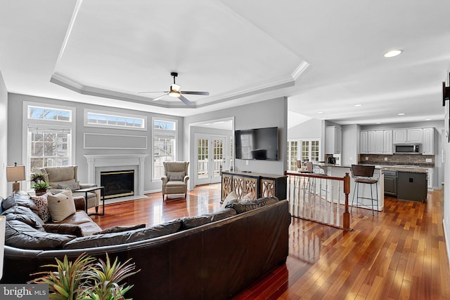 living room featuring crown molding, wood-type flooring, a raised ceiling, and ceiling fan