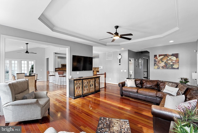 living room featuring a raised ceiling, ornamental molding, hardwood / wood-style flooring, and ceiling fan