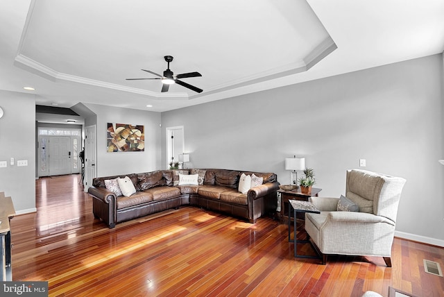 living room featuring a raised ceiling, crown molding, and hardwood / wood-style floors