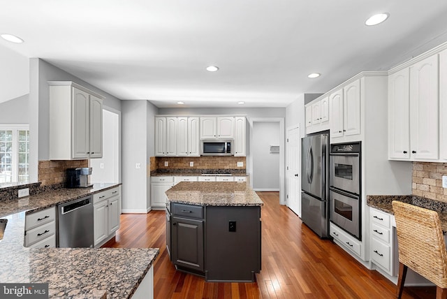 kitchen featuring white cabinetry, backsplash, dark stone counters, stainless steel appliances, and dark wood-type flooring