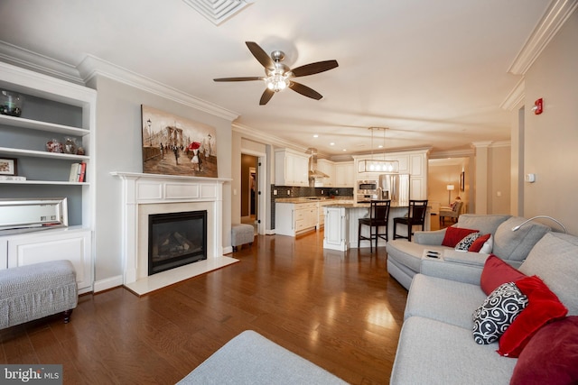 living room featuring visible vents, dark wood finished floors, ceiling fan, crown molding, and a fireplace