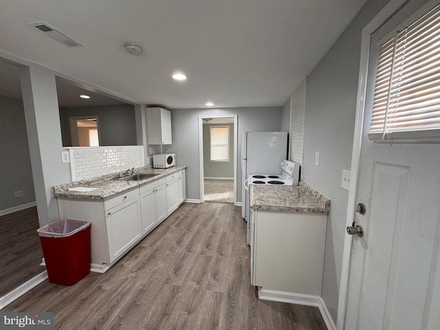 kitchen with white appliances, light hardwood / wood-style flooring, tasteful backsplash, light stone countertops, and white cabinets