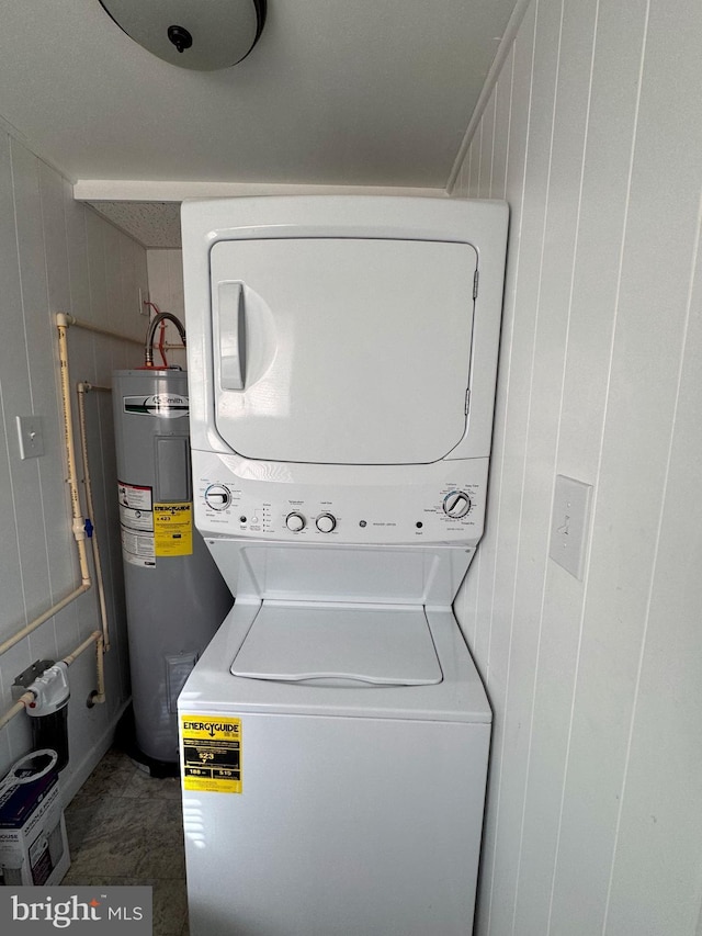 laundry room featuring electric water heater, wooden walls, and stacked washer and clothes dryer