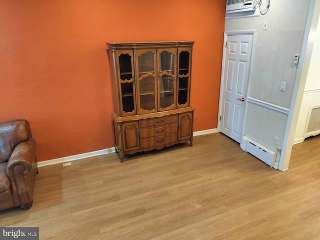 interior space featuring an AC wall unit, light hardwood / wood-style floors, and a baseboard heating unit