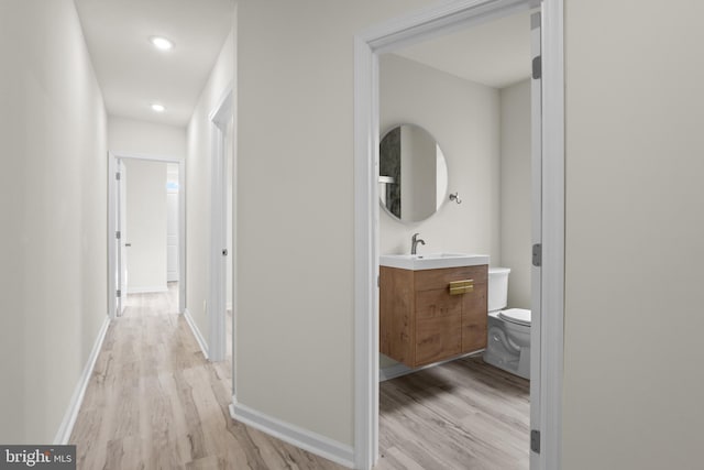 corridor with light wood-style floors, baseboards, and a sink