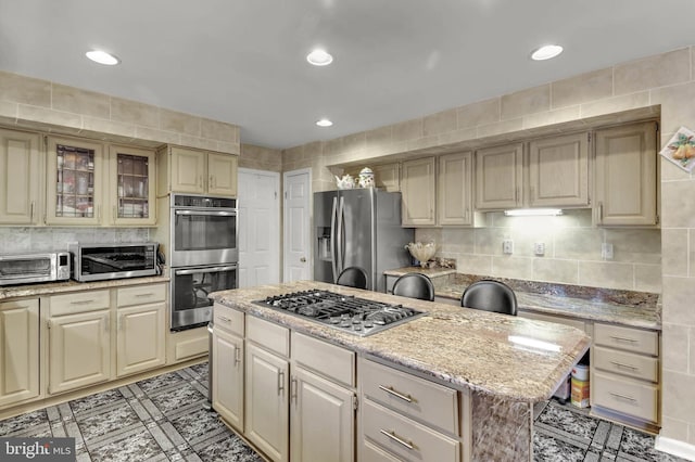 kitchen featuring light stone counters, a center island, tile walls, stainless steel appliances, and decorative backsplash