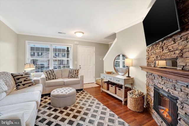 living room with hardwood / wood-style flooring, a stone fireplace, and crown molding