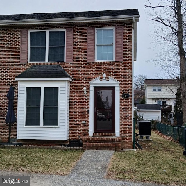 traditional home featuring cooling unit, brick siding, fence, and a front yard