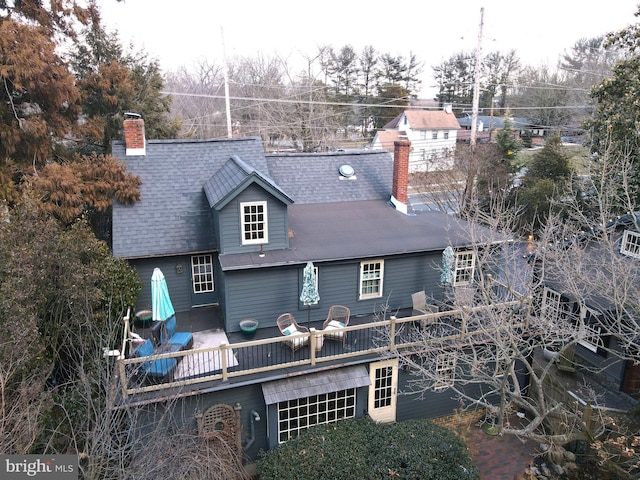 back of property featuring a deck, roof with shingles, and a chimney