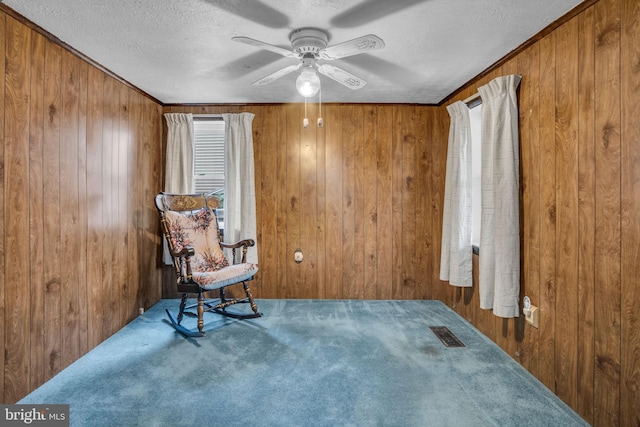 living area with ceiling fan, carpet, a textured ceiling, and wood walls