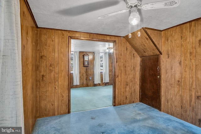 bonus room with ceiling fan, wooden walls, a textured ceiling, and carpet