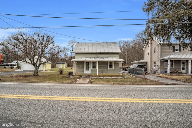 bungalow-style home with covered porch, a garage, an outdoor structure, a carport, and a front lawn