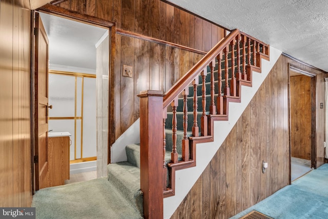 stairs with carpet flooring, a textured ceiling, and wood walls