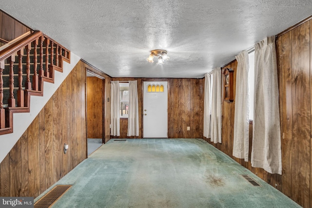 entrance foyer with carpet, a textured ceiling, and wooden walls