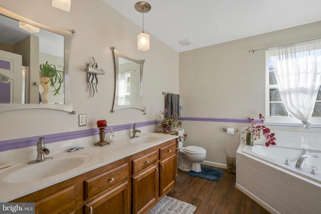 bathroom with wood-type flooring, tiled bath, vanity, and a wealth of natural light