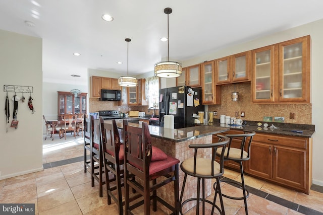 kitchen featuring a breakfast bar, black appliances, decorative backsplash, decorative light fixtures, and dark stone counters