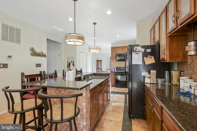 kitchen with a kitchen bar, tasteful backsplash, a center island with sink, pendant lighting, and black appliances