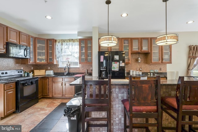 kitchen featuring tasteful backsplash, sink, a kitchen breakfast bar, hanging light fixtures, and black appliances