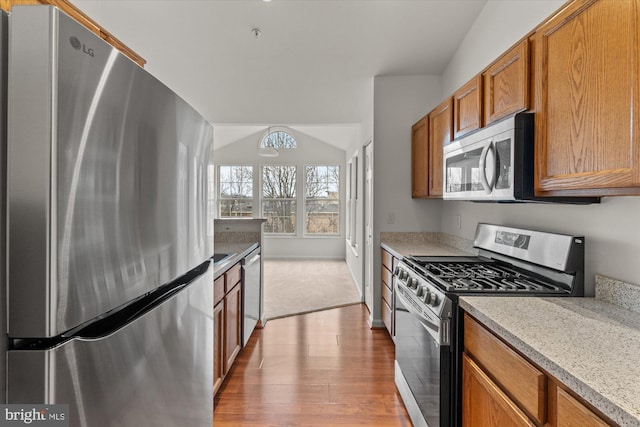 kitchen featuring lofted ceiling, appliances with stainless steel finishes, light stone countertops, and light hardwood / wood-style flooring