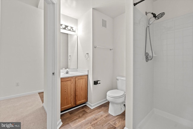 bathroom featuring vanity, hardwood / wood-style floors, toilet, and a tile shower