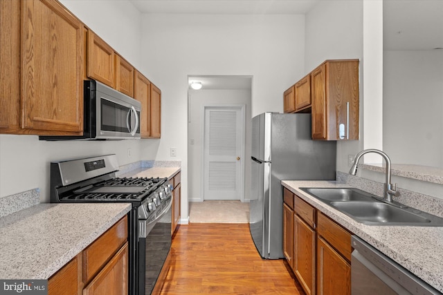 kitchen featuring stainless steel appliances, sink, light stone counters, and light wood-type flooring