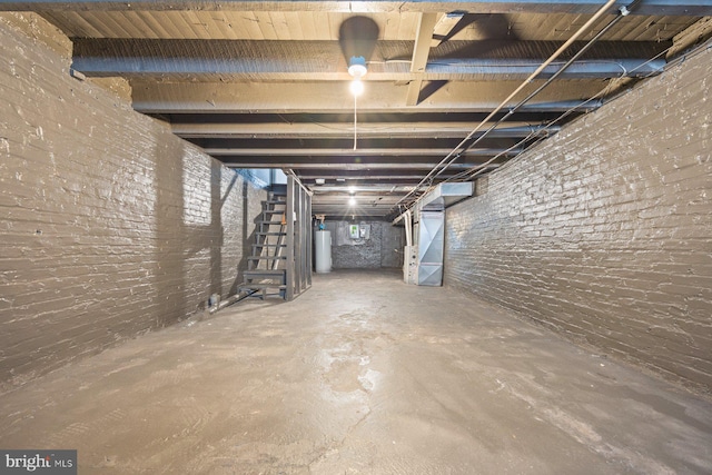 basement featuring heating unit, water heater, and brick wall