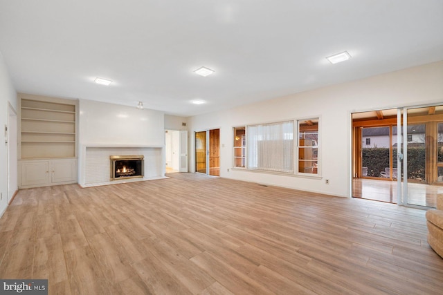 unfurnished living room with a brick fireplace, built in shelves, light hardwood / wood-style flooring, and a healthy amount of sunlight