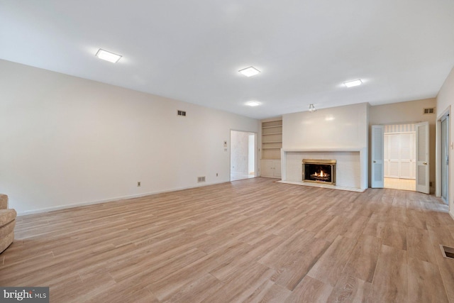 unfurnished living room with built in features, a fireplace, and light hardwood / wood-style flooring